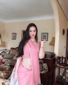 a woman in a pink sari is standing in a living room with pictures on the wall