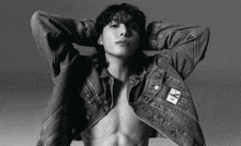 a black and white photo of a shirtless man wearing a denim jacket with the letters ck on it