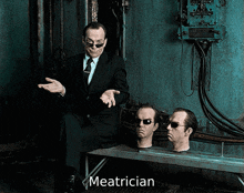 a man in a suit and tie is sitting next to two mannequin heads with the name meatrician on the bottom right