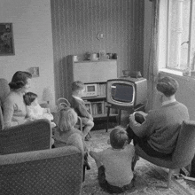 a black and white photo of a family watching a tv