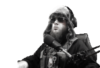 a man with a beard is sitting in front of a microphone wearing a fur hat and sunglasses .