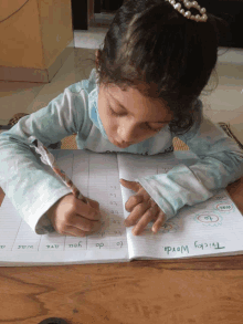 a little girl is writing in a notebook that has tricky words written on it