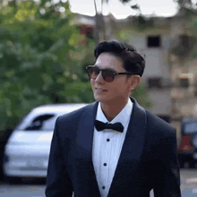 a man wearing sunglasses and a tuxedo is walking down the street