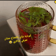 a glass filled with red liquid and green leaves with arabic writing on it