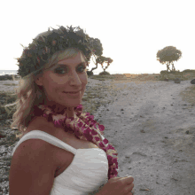 a woman wearing a lei and a flower crown stands on a beach