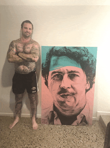 a shirtless man stands next to a painting of a man with a bandana on his head