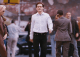 a man in a white shirt and black pants walks down a street