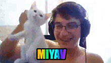 a man wearing headphones holds a white cat with the name miyav on the bottom