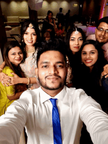 a man in a white shirt and blue tie takes a selfie with a group of people