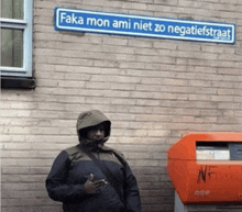 a man in a hooded jacket is standing under a sign that says ' fika mon ami niet zo negativiststraat '