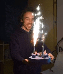 a man is holding a birthday cake with candles and fireworks on it .