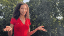 a woman in a red shirt stands in front of a forest