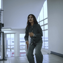 a woman wearing a denim jacket and jeans is dancing in a hallway