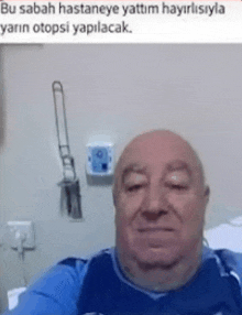 a bald man is taking a selfie in a hospital room while wearing a blue shirt .