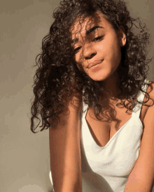 a woman with curly hair is wearing a white top