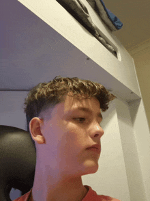 a young man with curly hair is sitting in a chair under a bunk bed