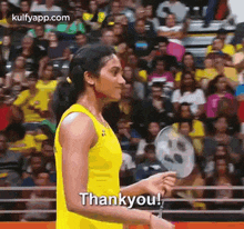 a woman in a yellow tank top is holding a badminton racket in front of a crowd and saying thank you .