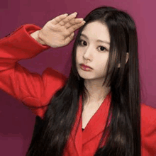 a woman with long black hair wearing a red jacket is saluting .