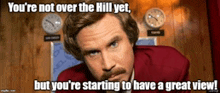 a man with a mustache is sitting in front of two clocks and a sign that says you 're not over the hill yet