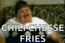 a fat man is sitting on a couch with a mustache and eating chili cheese fries .
