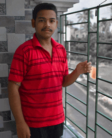 a young man wearing a red striped shirt stands on a balcony