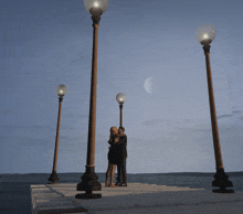 a man and woman are kissing on a dock with a crescent moon in the background