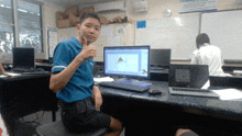 a boy in a blue shirt is giving a thumbs up in front of a dell computer