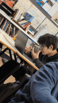 a boy sitting at a desk using a laptop and a cell phone