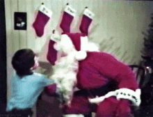 a man in a santa suit is standing next to a child in front of stockings hanging on the wall .