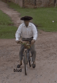 a man wearing a sombrero is riding a bike on a dirt road with the word blud written below him