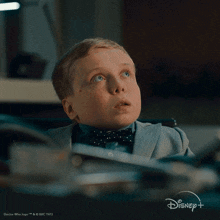 a young boy in a suit and bow tie is sitting at a desk with a disney logo in the background