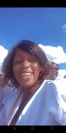 a woman in a white shirt smiles in front of a blue sky and clouds