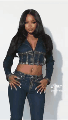 a woman in a crop top and jeans is standing in front of a white wall .