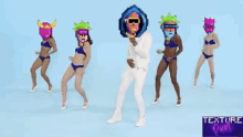 a group of women in bikinis are dancing with a man in a white suit with a mask on his head ..