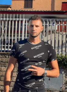 a man wearing a black balenciaga shirt stands in front of a building