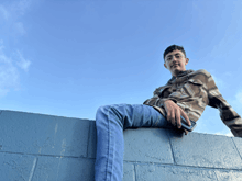 a man in a plaid shirt sits on a blue wall