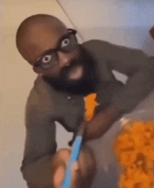 a man with glasses and a beard is eating a slice of cheese with a knife .