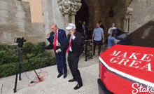 a man in a suit and tie is dancing in front of a red make america great again car .