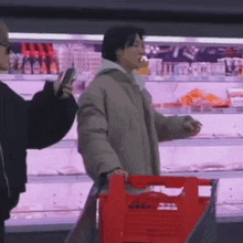 a man is pushing a red shopping cart in a supermarket while another man takes a picture of him .