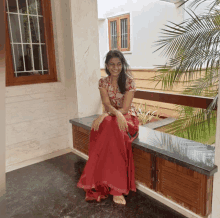 a woman in a red skirt sits on a ledge in front of a window