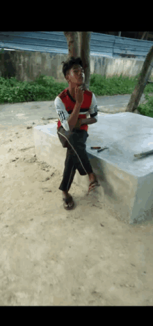 a young man sits on a concrete bench with his hand on his chin