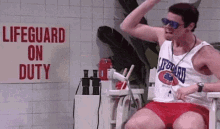 a man in a lifeguard uniform is sitting in a chair in front of a sign that says `` lifeguard on duty '' .