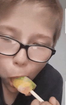 a boy wearing glasses is licking a lollipop