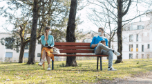 a man and a woman wearing face masks are sitting on a park bench