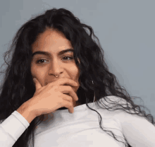 a woman with long curly hair is covering her mouth with her hand and wearing a nose ring .