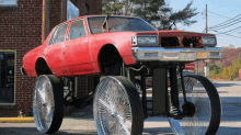 a red car with big wheels is parked in front of a brick building with a license plate that says ' r '