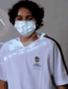 a young man wearing a mask and a white shirt is standing in a room .