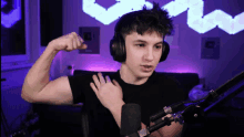 a young man wearing headphones and a black shirt flexes his muscles in front of a microphone