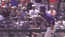 a baseball player in a purple uniform is standing in front of a crowd of people at a baseball game .