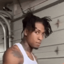 a man wearing a white tank top is standing in front of a garage door .